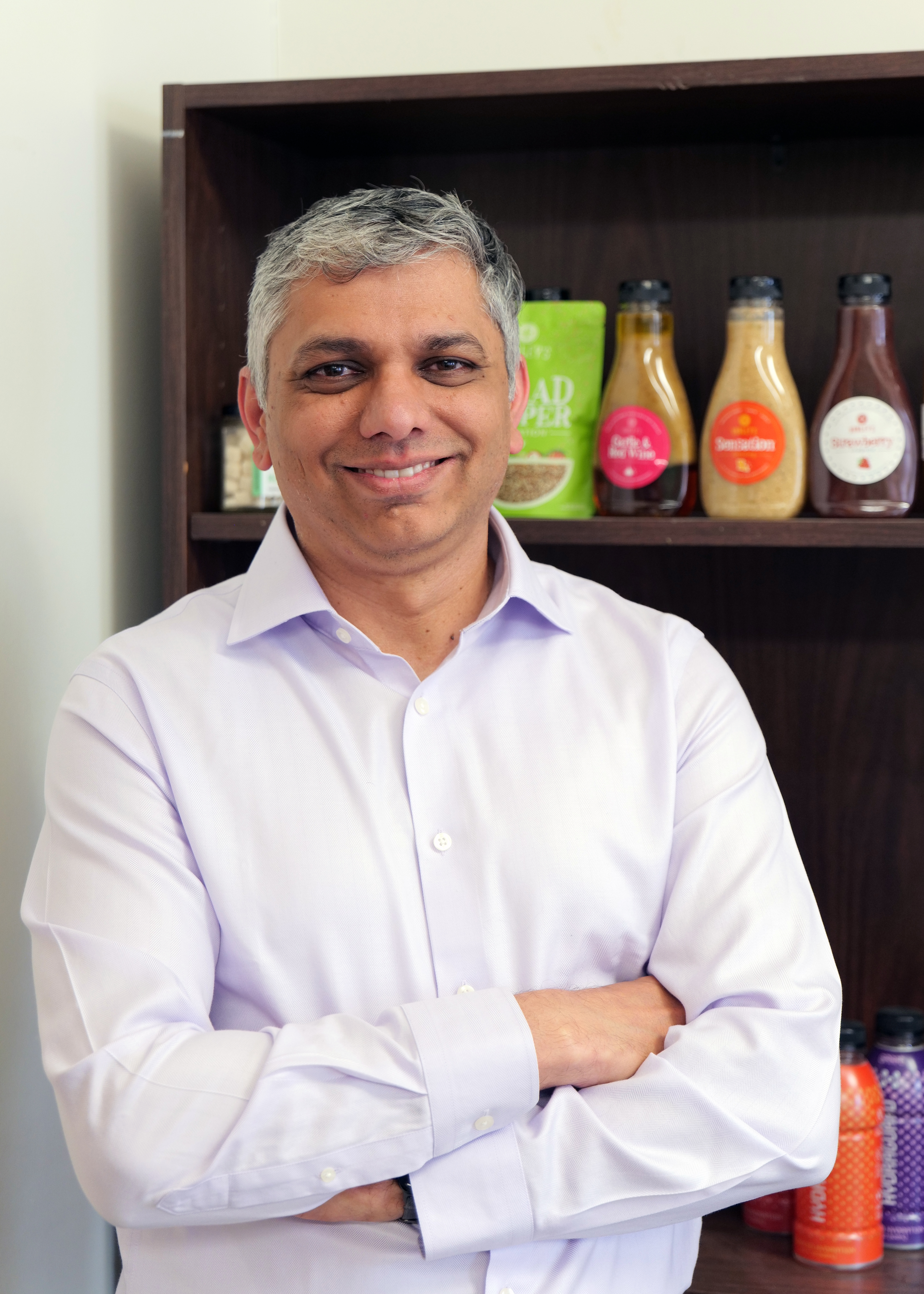 A man crosses his arms and poses in front of a shelf. 